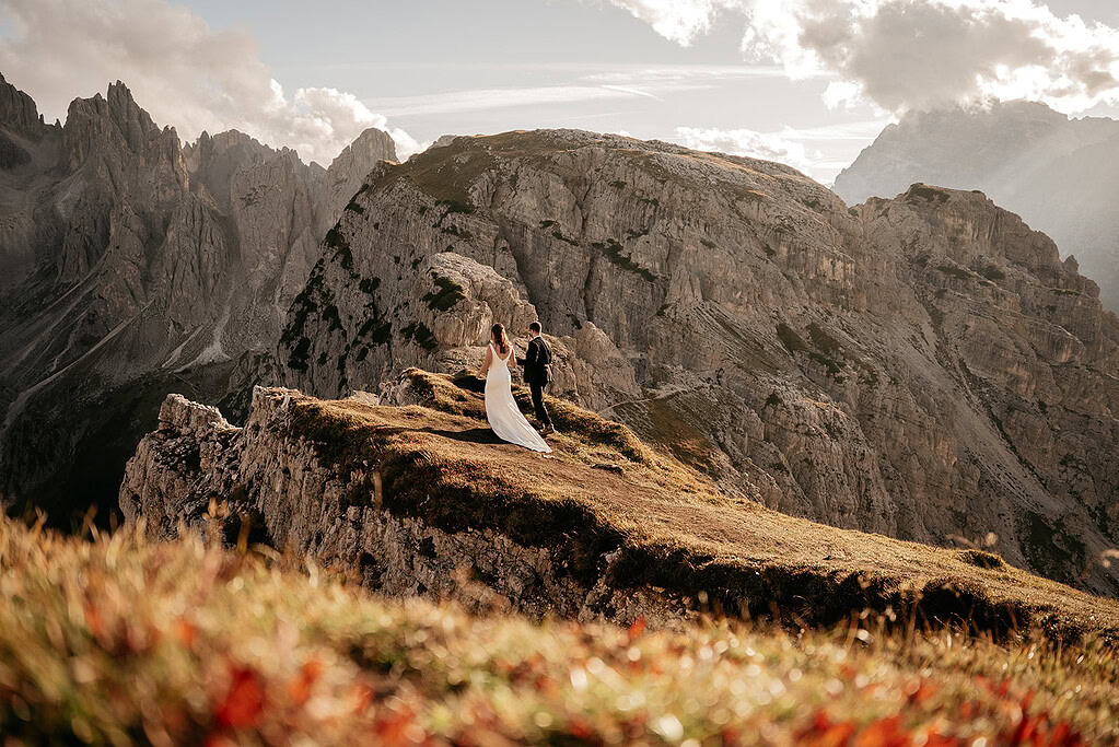 Bride and groom standing on mountain cliff.