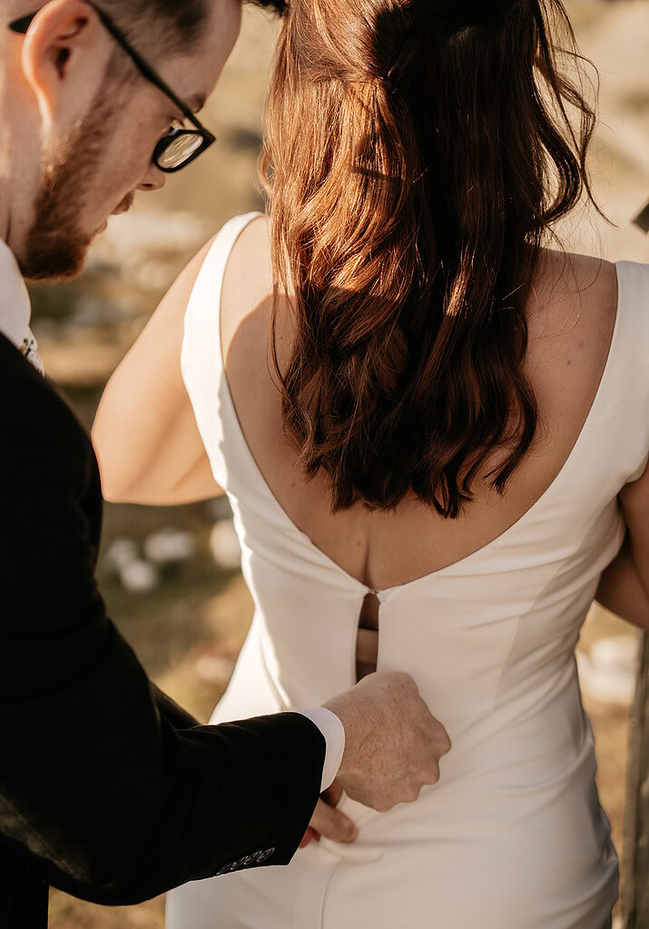 Man fastening back of woman's wedding dress