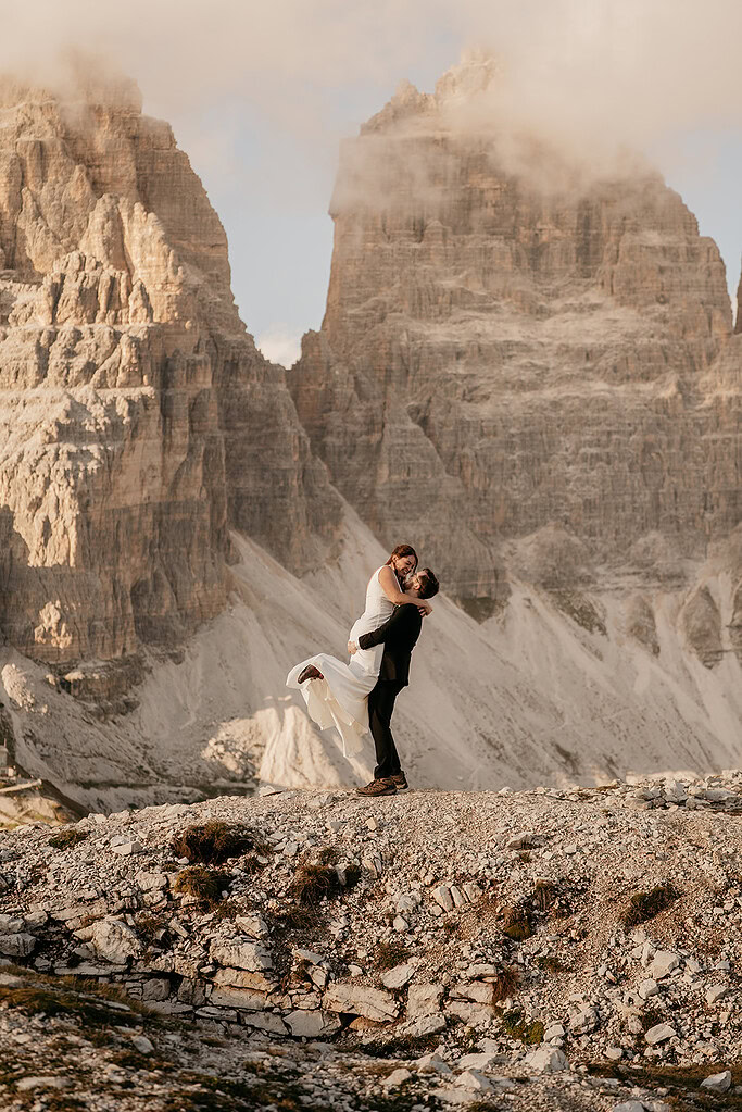 Couple embraces beside rugged mountain landscape.