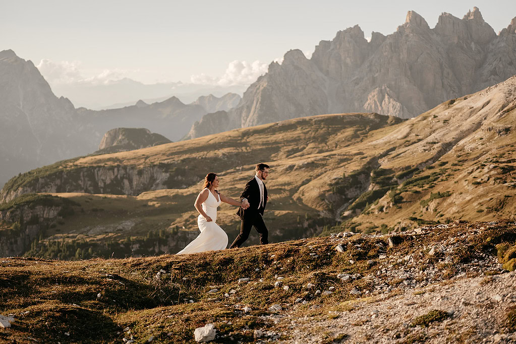 Bride and groom walking on mountain trail.