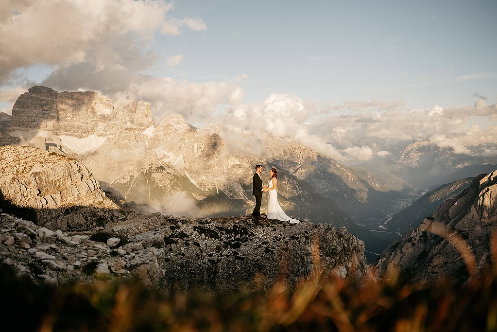 Couple standing on mountain with scenic backdrop.