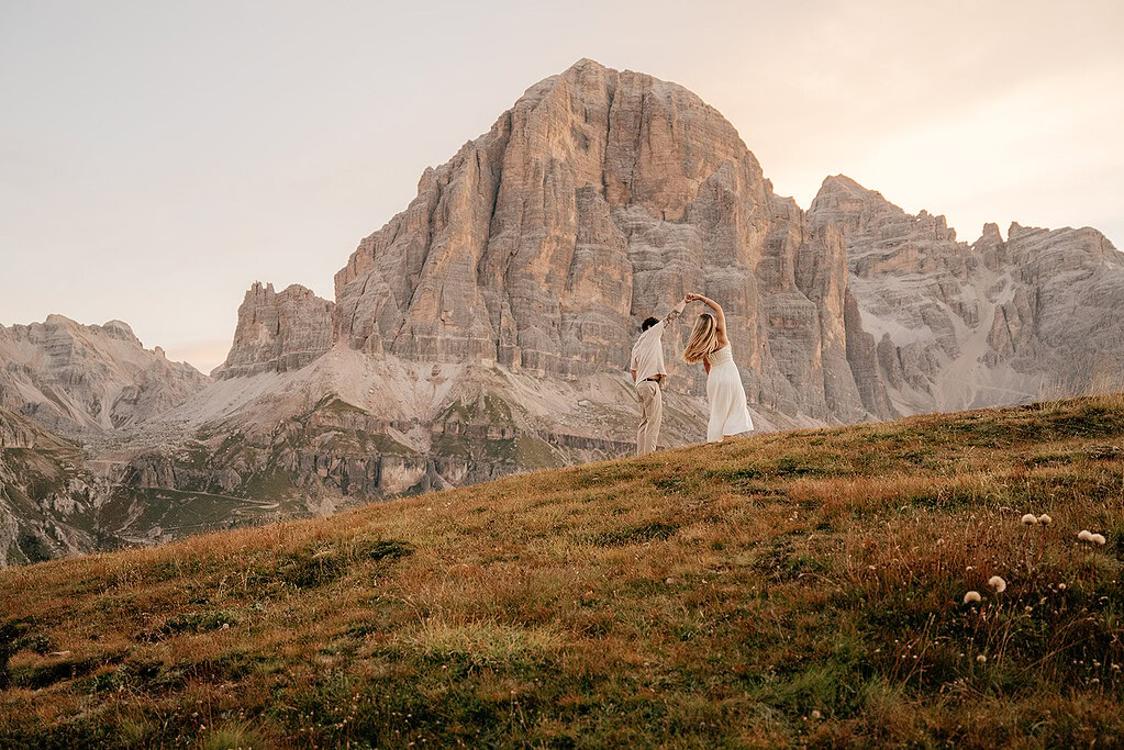 Couple dancing on hill with mountains at sunset.