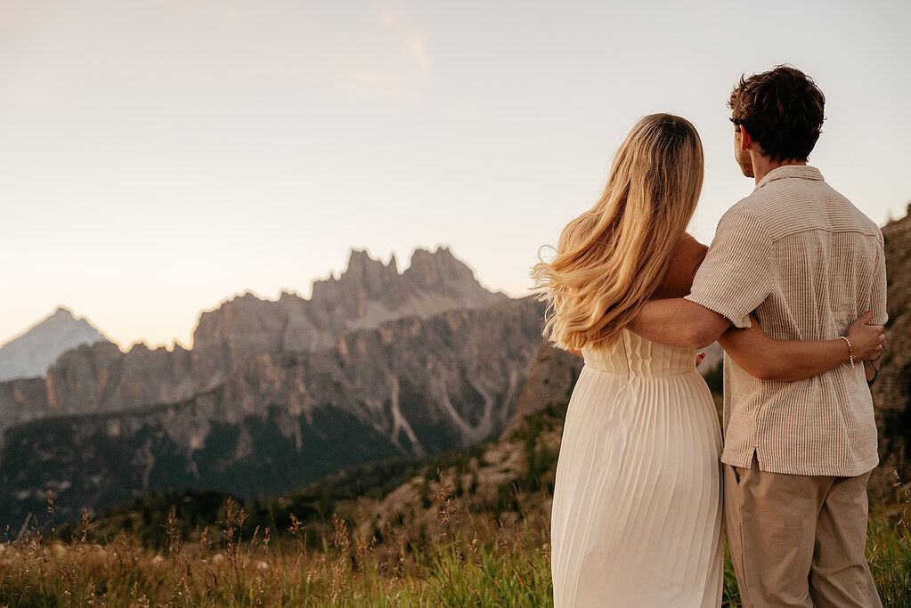 Couple embraces, admiring mountain sunset scenery.