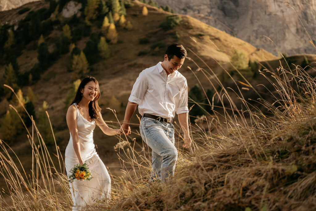 Couple walking hand in hand on grassy hill.