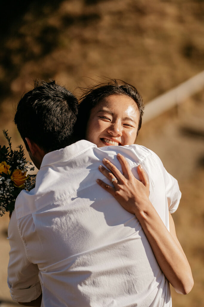 Smiling woman hugging man with flowers outdoors.