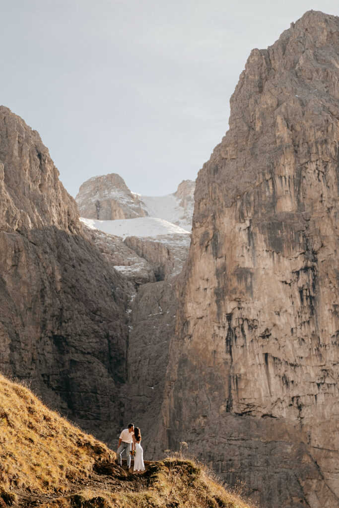 Couple kisses on mountain path with towering cliffs.