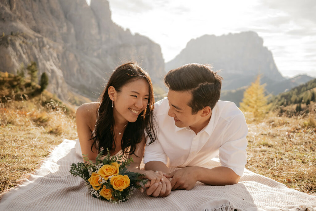 Couple smiling outdoors with yellow roses bouquet.