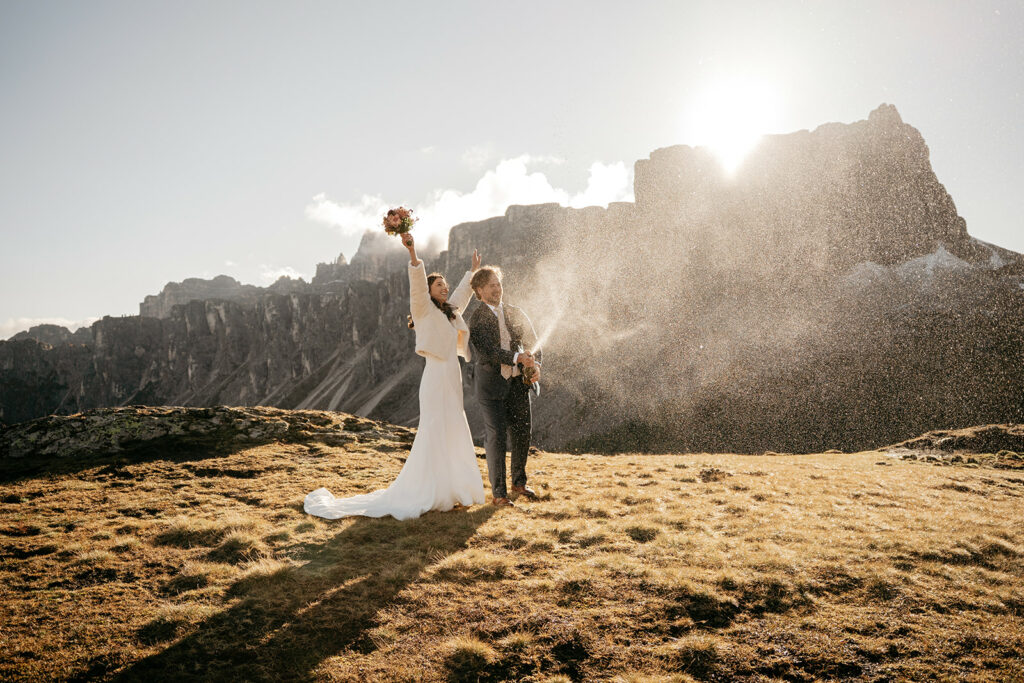 Couple celebrating outdoors with mountains and champagne spray.