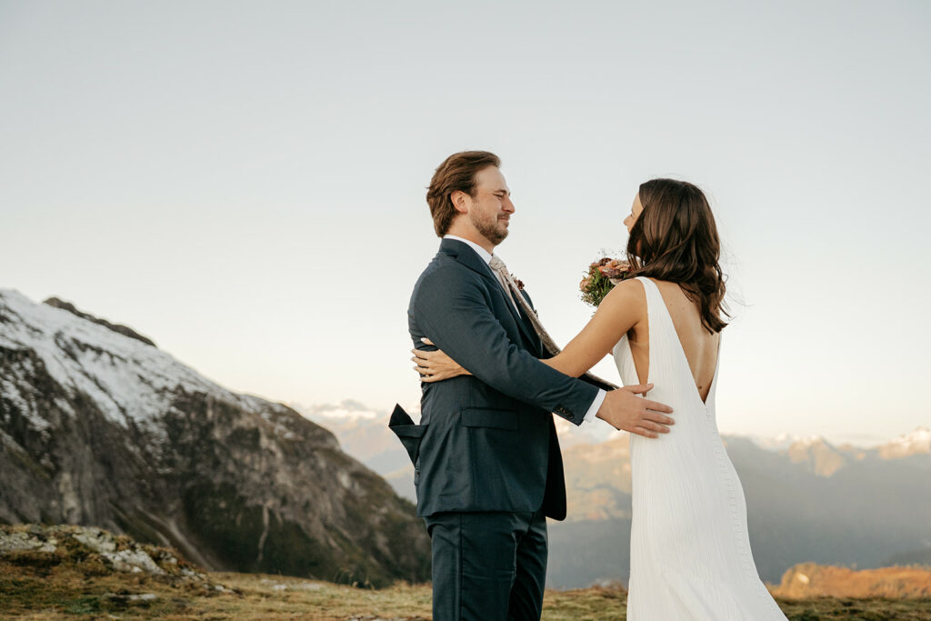 Bride and groom embrace on snowy mountaintop