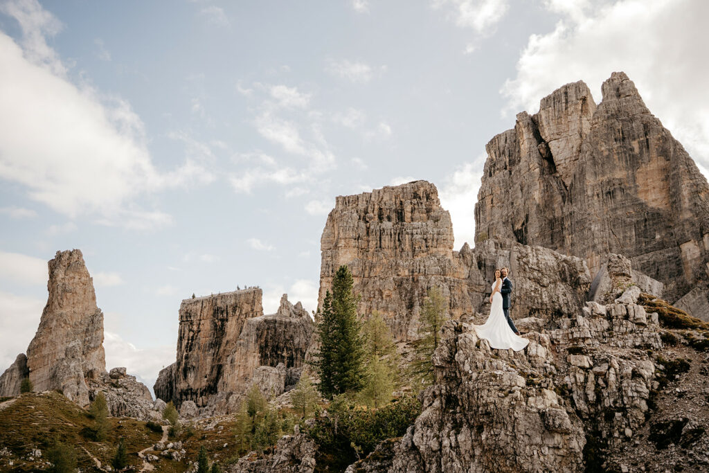 Couple standing on rocky mountain peak with cliffs.