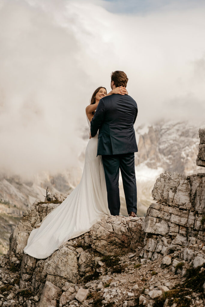 Bride and groom embracing on rocky mountain cliff.