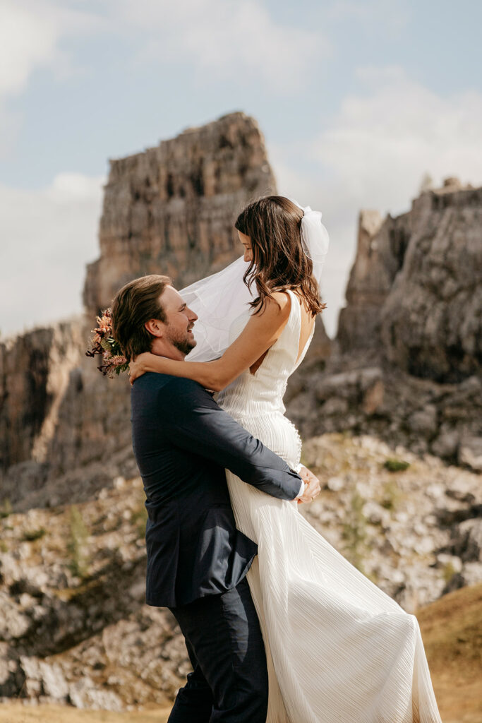 Bride and groom embrace in mountain landscape.
