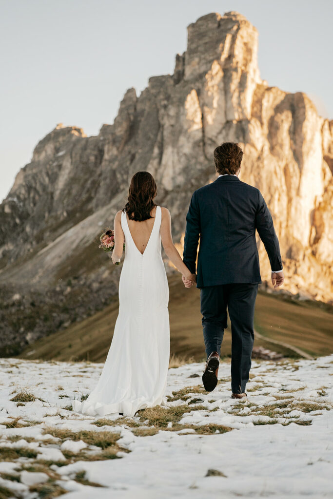 Couple in wedding attire walking toward mountain scenery.