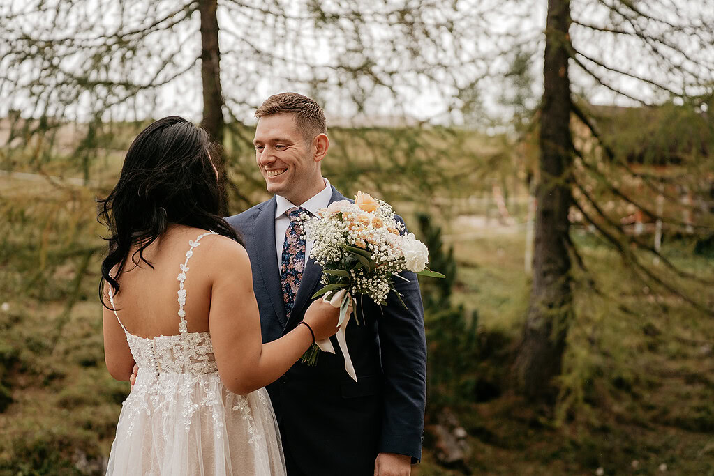 Bride and groom smiling with bouquet outdoors.