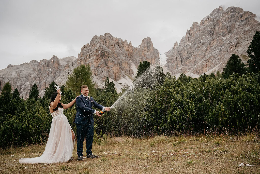 Couple celebrating with champagne in mountain scenery.
