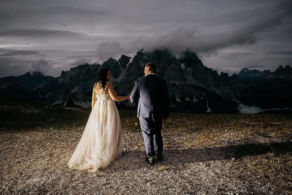 Couple in wedding attire walking in mountains at dusk.