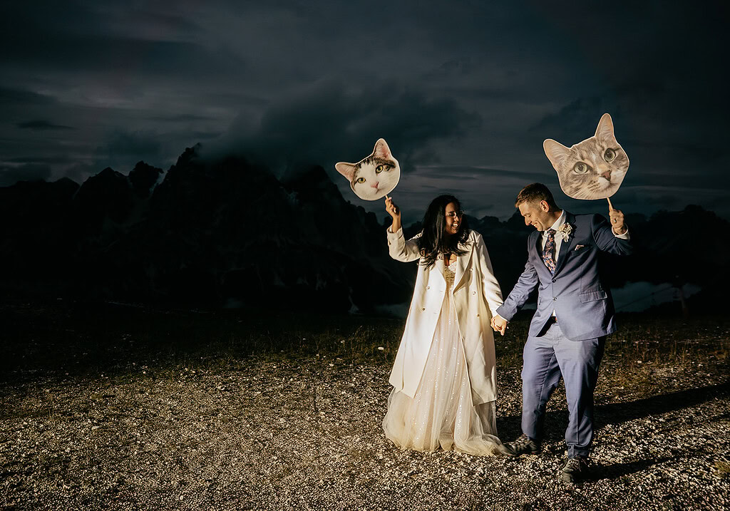 Couple holding cat face signs outdoors at night.