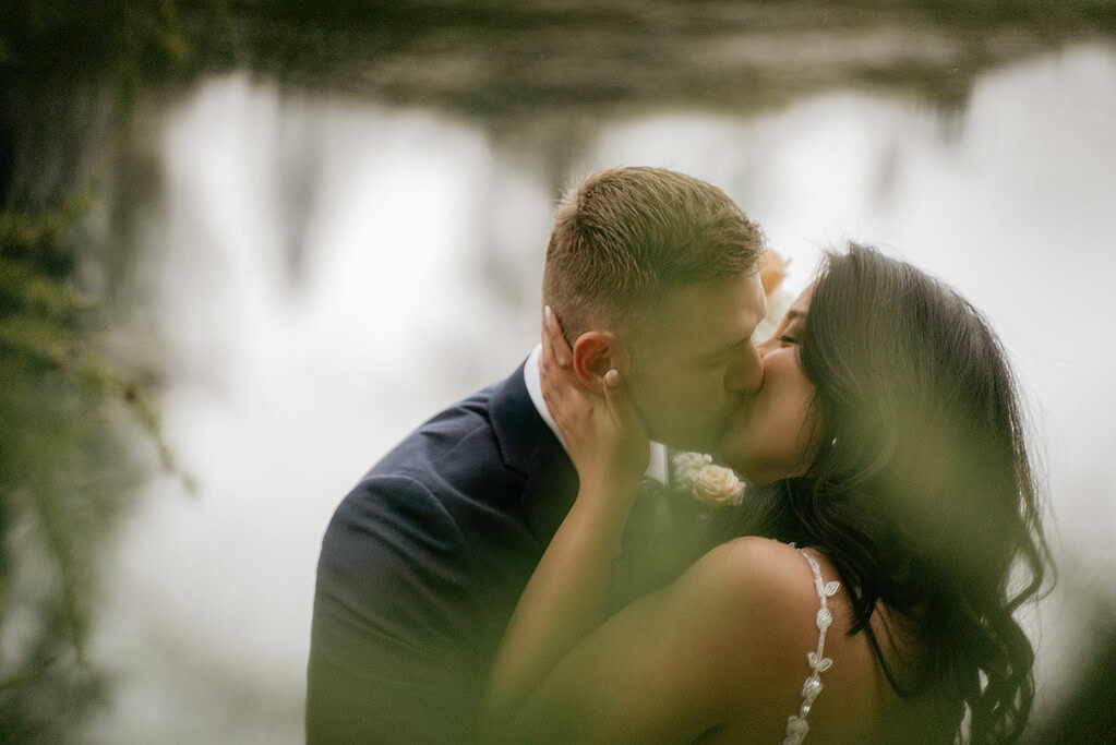 Couple kissing by a lake on their wedding day.