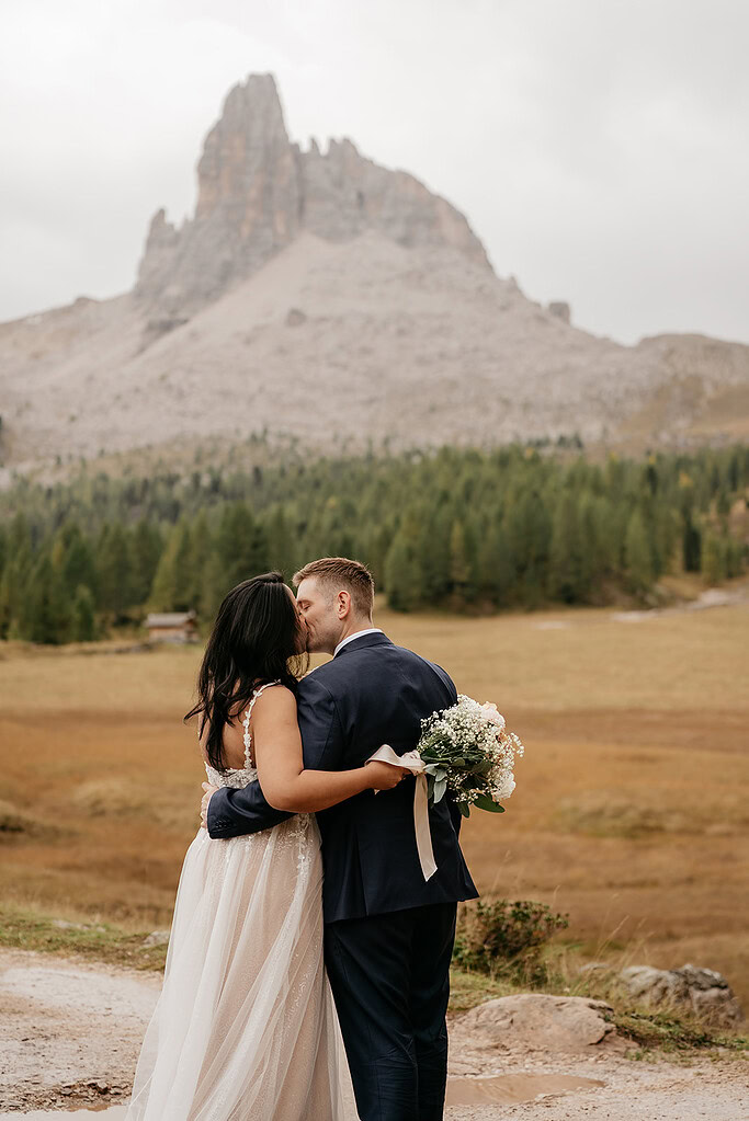 Bride and groom embrace with mountain backdrop.