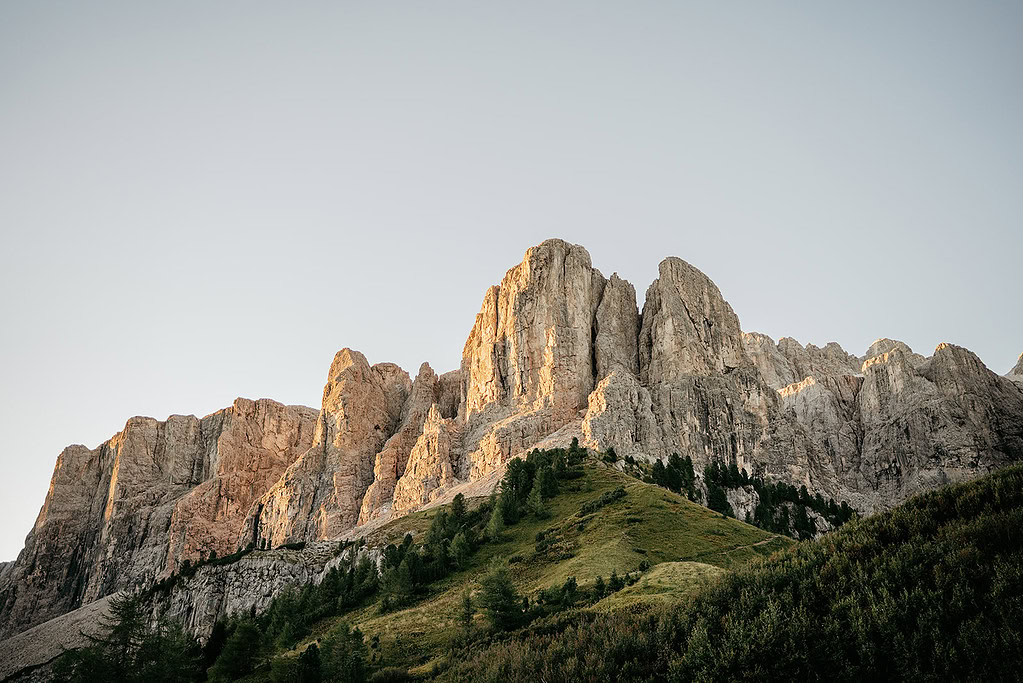 Sunlit rocky mountain peak with lush green slopes.