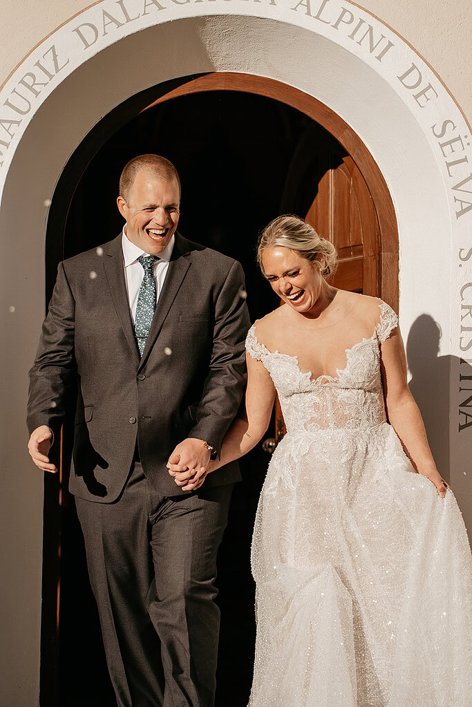 Smiling couple exits church after wedding ceremony.