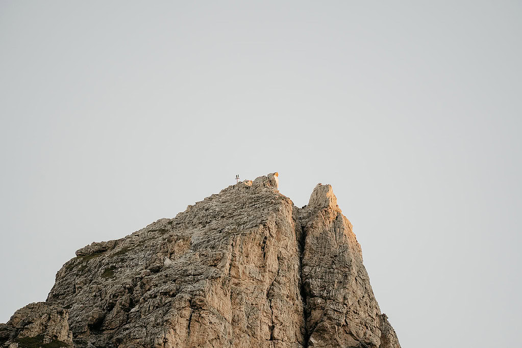 Climbers reach rocky mountain peak at sunset.