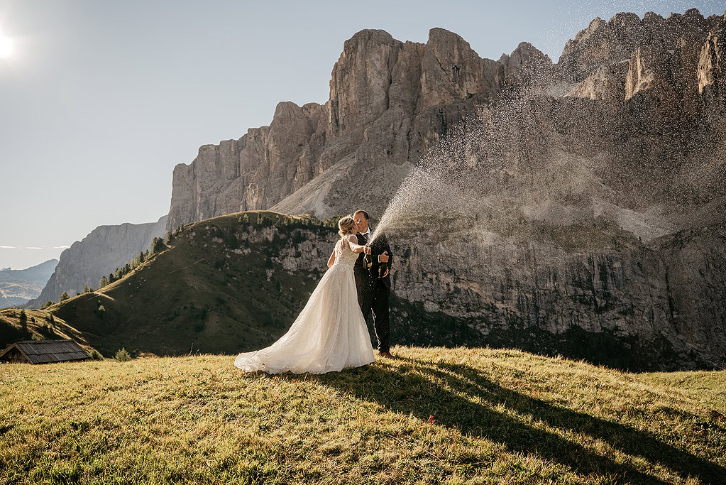 Bride and groom celebrating with champagne in mountains.