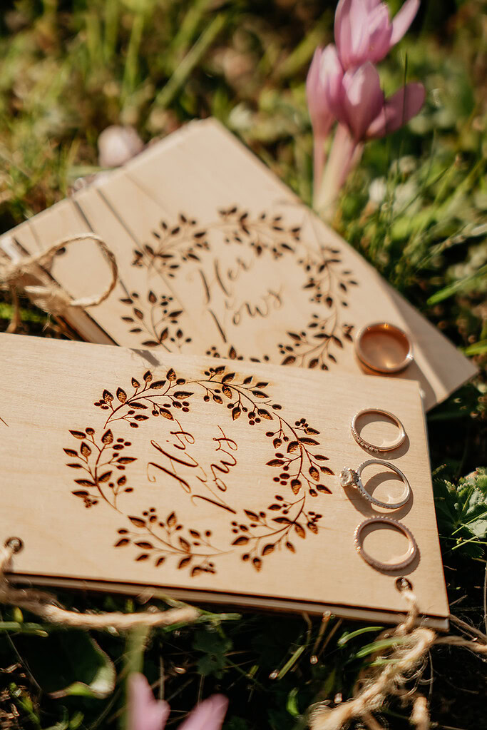 Wooden vow booklets with wedding rings on grass.