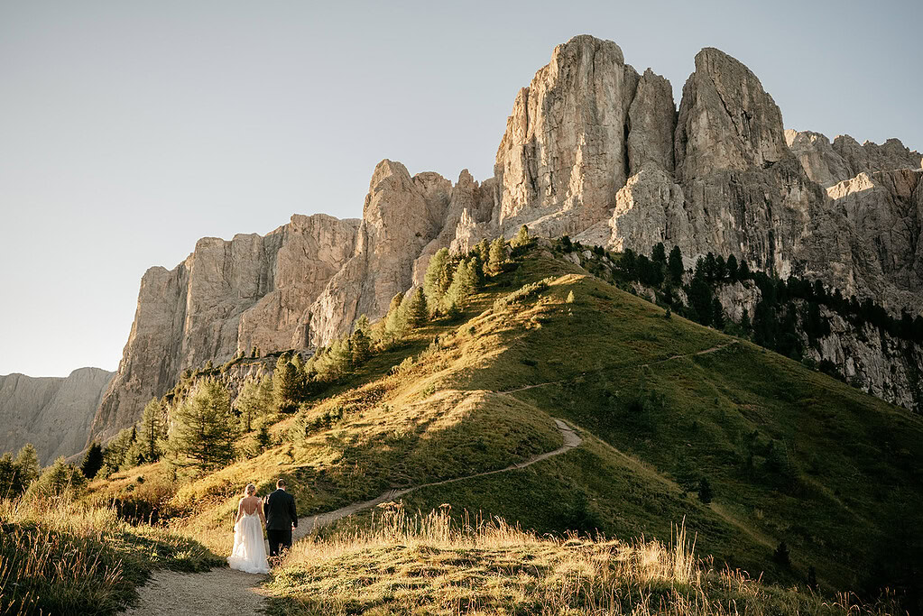 Couple walking mountain path, rocky cliffs background.